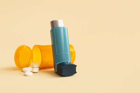 Asthma inhaler and pills on beige background