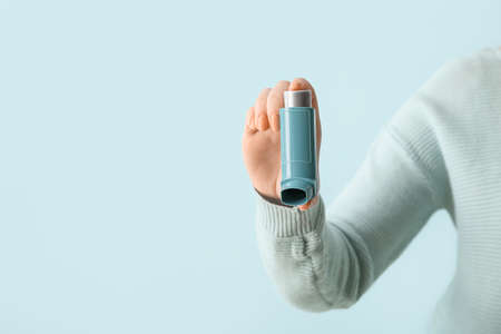 Woman holding asthma inhaler on blue background