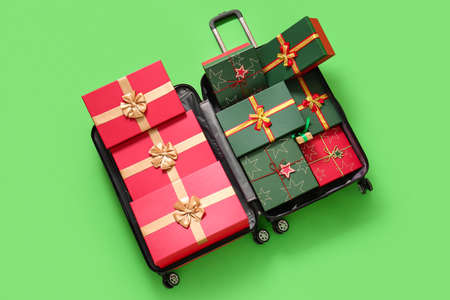Open suitcase with Christmas gift boxes on green background