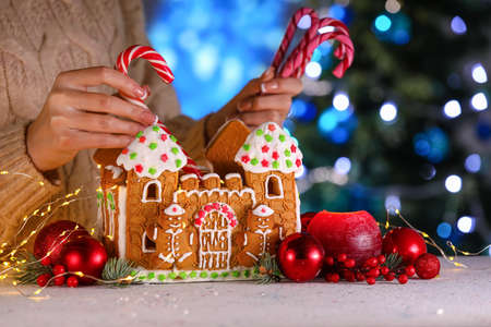 Woman putting treats into gingerbread house at table, closeupの写真素材