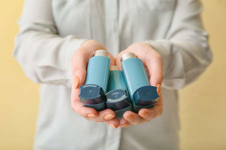 Woman holding asthma inhaler on beige background