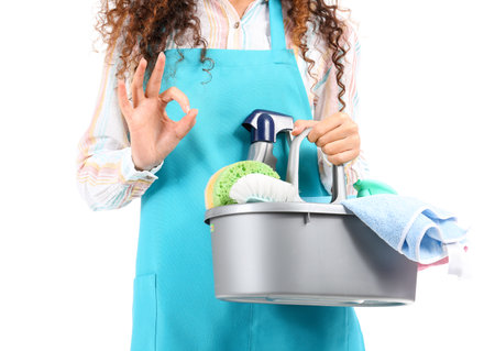 Young female worker of cleaning service with supplies in bucket on white background, closeupの写真素材