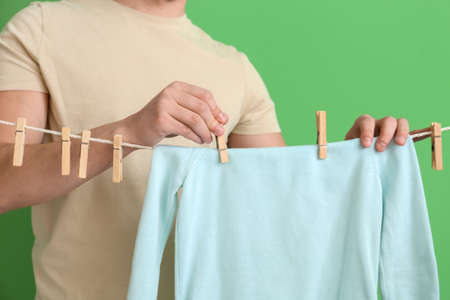 Young man hanging children's sweatshirt with clothespins on green background, closeupの写真素材