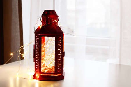 Christmas lantern with beautiful glowing lights on table in roomの写真素材