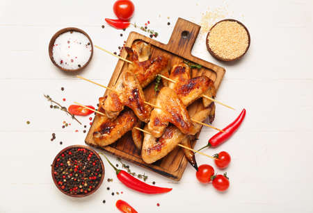 Wooden board with grilled chicken wings skewers on white wooden backgroundの写真素材