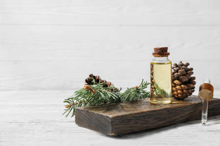 Board with bottle of essential oil, pine cones and fir branch on light wooden backgroundの写真素材