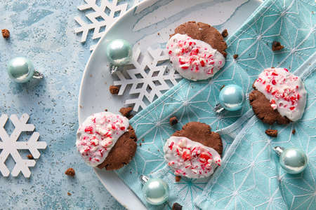 Plate with tasty candy cane cookies and Christmas decor on blue background, closeup