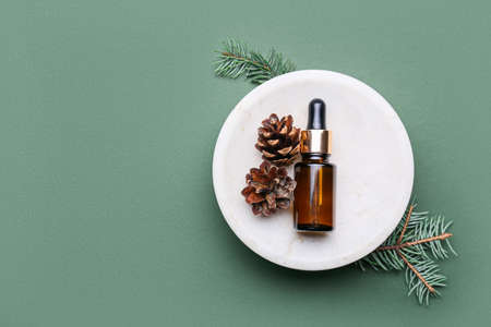 Plate with bottle of essential oil, pine cones and fir branches on green backgroundの写真素材