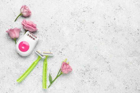 Modern epilator, flowers and razors on light grunge background