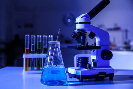 Modern microscope and conical flask with liquid on table in medical laboratoryの写真素材