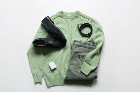 Stylish male sweater, pants, shoes, belt and earphones on light background
