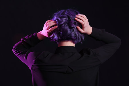 Beautiful young woman with violet hair on black background, back view. Very Peri - color of year 2022の写真素材
