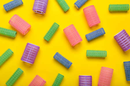 Set of different hair curlers on yellow background