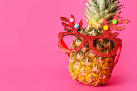 Funny pineapple in Christmas glasses on pink backgroundの写真素材