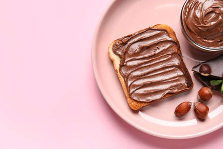 Plate of bread with chocolate paste and hazelnuts on pink background, closeup