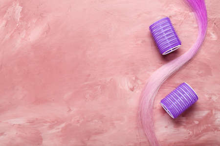 Pink hair strand with curlers on grunge background