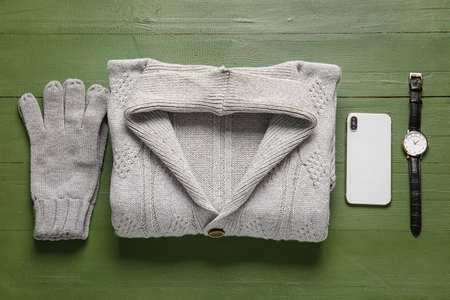Male sweater, gloves, wristwatch and mobile phone on green wooden background
