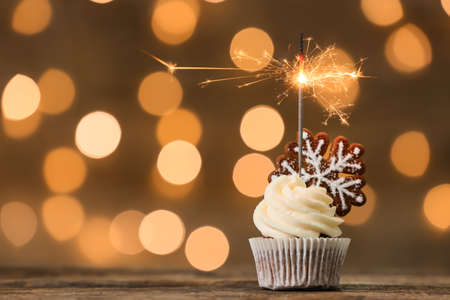 Tasty Christmas cupcakes with gingerbread cookies and sparkler on table against blurred backgroundの写真素材