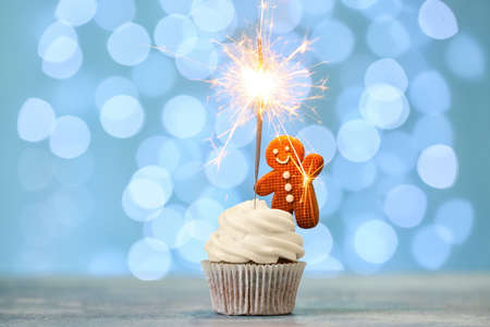 Tasty Christmas cupcakes with gingerbread cookies and sparkler on table against blurred backgroundの写真素材