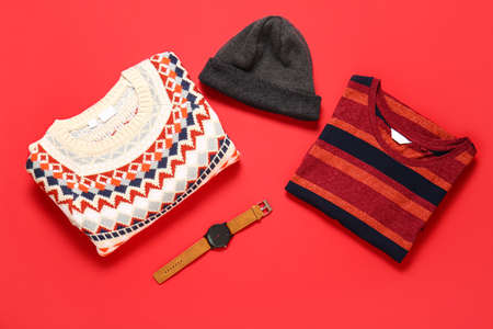 Male sweaters, hat and wristwatch on red background