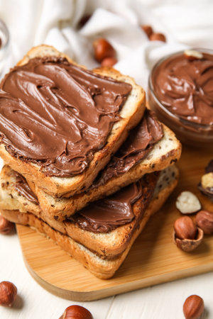 Board of bread with chocolate paste and hazelnuts on table, closeupの写真素材