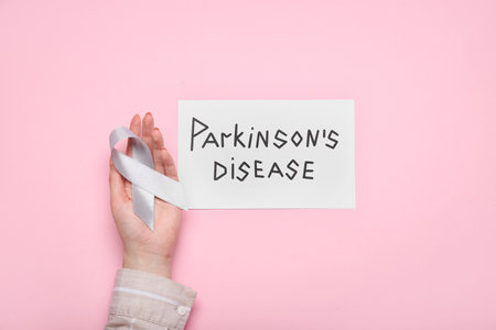 Paper with text PARKINSON'S DISEASE, female hand and awareness ribbon on pink backgroundの写真素材