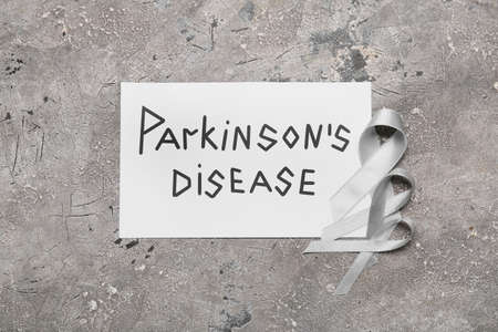 Paper sheet with text PARKINSON'S DISEASE and awareness ribbons on grunge backgroundの写真素材