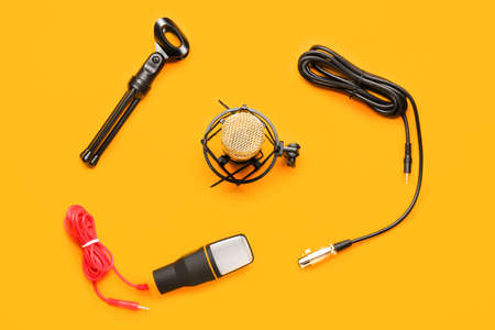 Modern microphones with stand and wires on orange background