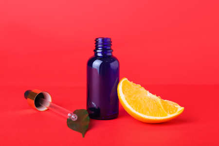 Bottle of essential oil and fresh cut orange on red background, closeupの写真素材