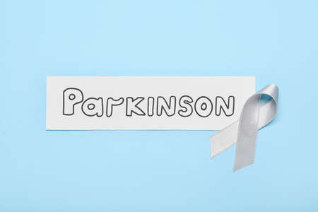 Paper with word PARKINSON and awareness ribbon on blue background