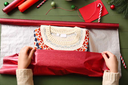 Woman making beautiful Christmas gift on color wooden table