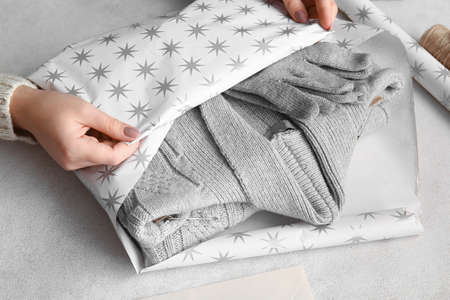 Woman wrapping stylish gloves and sweater on tableの写真素材