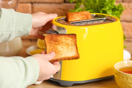 Woman with bread slice near yellow toaster in kitchen, closeup