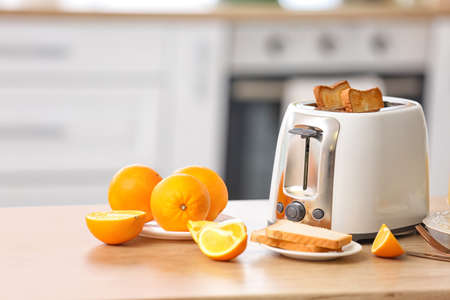 White toaster with bread slices and oranges on table in light kitchenの写真素材