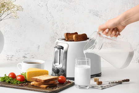 Woman pouring milk into glass near toaster in kitchenの写真素材
