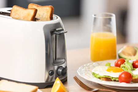 White toaster with tasty breakfast on table in light kitchen