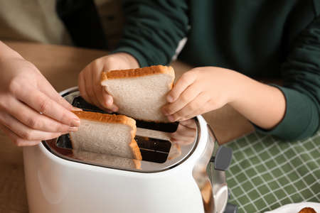Little boy and his mother putting bread slices into toaster in kitchen, closeup