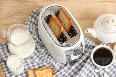 White toaster with bread slices and drinks on wooden tableの写真素材