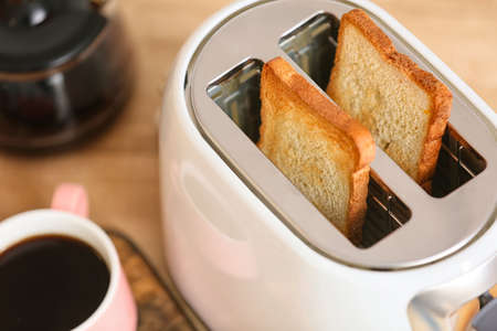 White toaster with bread slices and cup of coffee on table, closeup