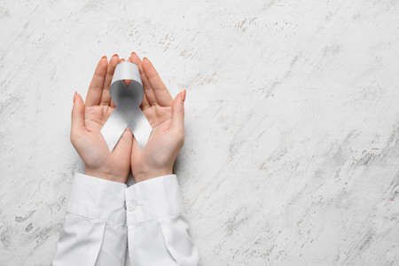 Female hands with Parkinson's awareness ribbon on light background