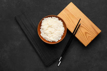 Bowl with tasty boiled rice, chopsticks and mat on dark backgroundの写真素材
