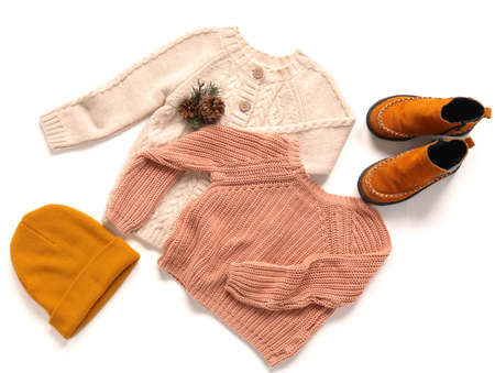 Stylish sweaters, hat, shoes and winter decor on light background