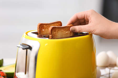 Woman taking bread slice from yellow toaster in kitchen, closeupの写真素材