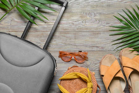 Female accessories for travelling, suitcase and palm leaves on gray wooden background
