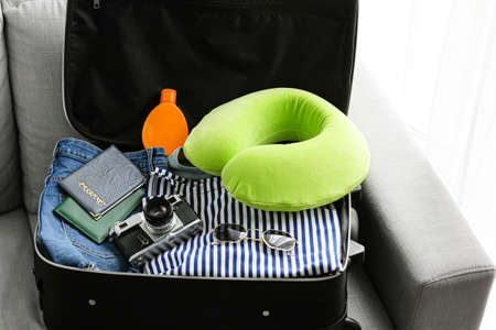 Opened suitcase with traveler accessories on sofa