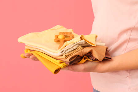 Pregnant woman with stack of baby clothes and rattle on pink background, closeupの写真素材