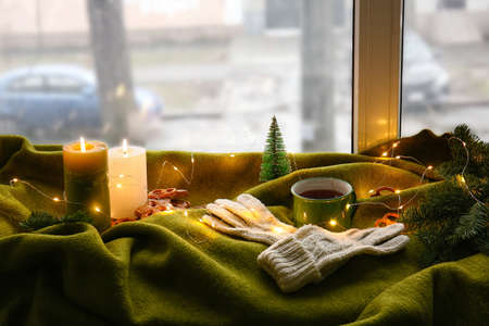 Warm gloves with cup of tea, burning candles and plaid on windowsillの写真素材