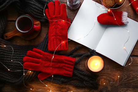 Warm gloves, scarf, cup of tea, blank book and burning candle on wooden backgroundの写真素材