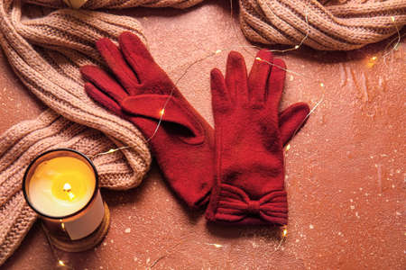 Warm gloves, scarf, Christmas lights and burning candle on red backgroundの写真素材