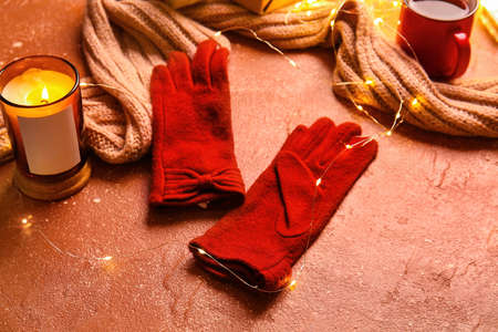 Warm gloves, scarf, Christmas lights and burning candle on red backgroundの写真素材